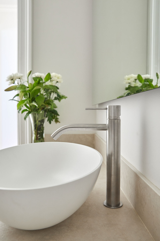 Tall brushed stainless basin mixer beside a white vessel basin