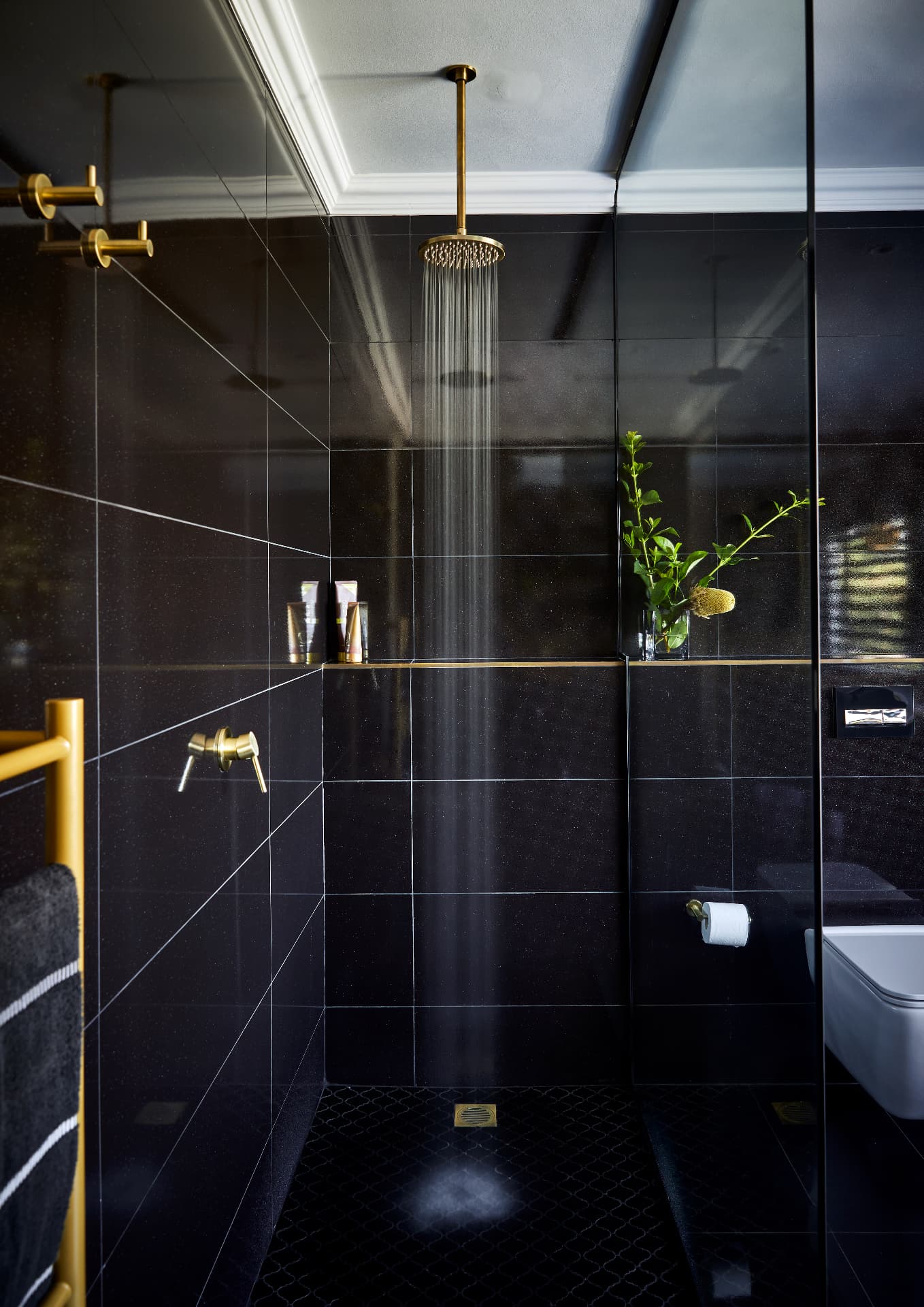 Brass ceiling rain shower head in a black-tiled luxury bathroom in Hout Bay