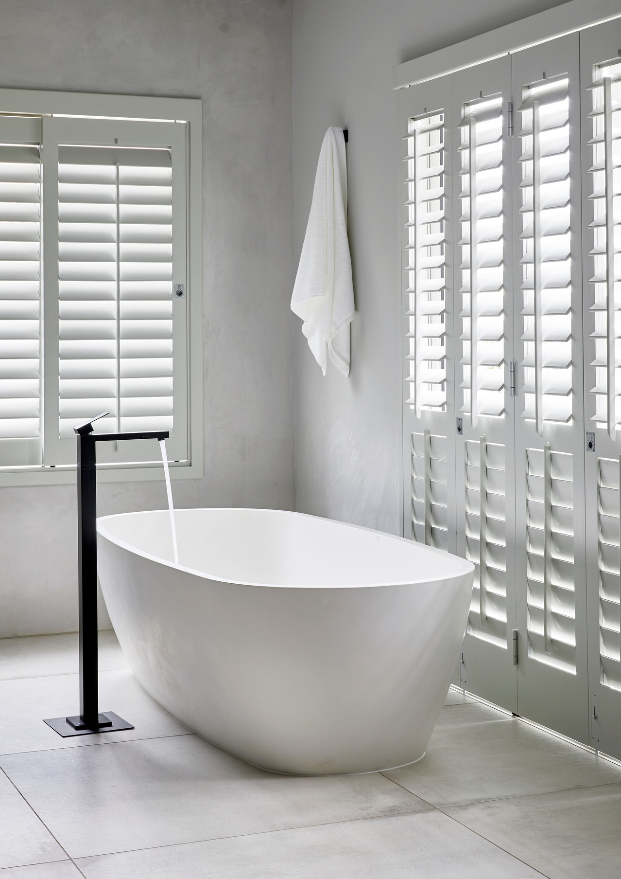 Matte black floor-mounted freestanding bath mixer beside a white stone bath